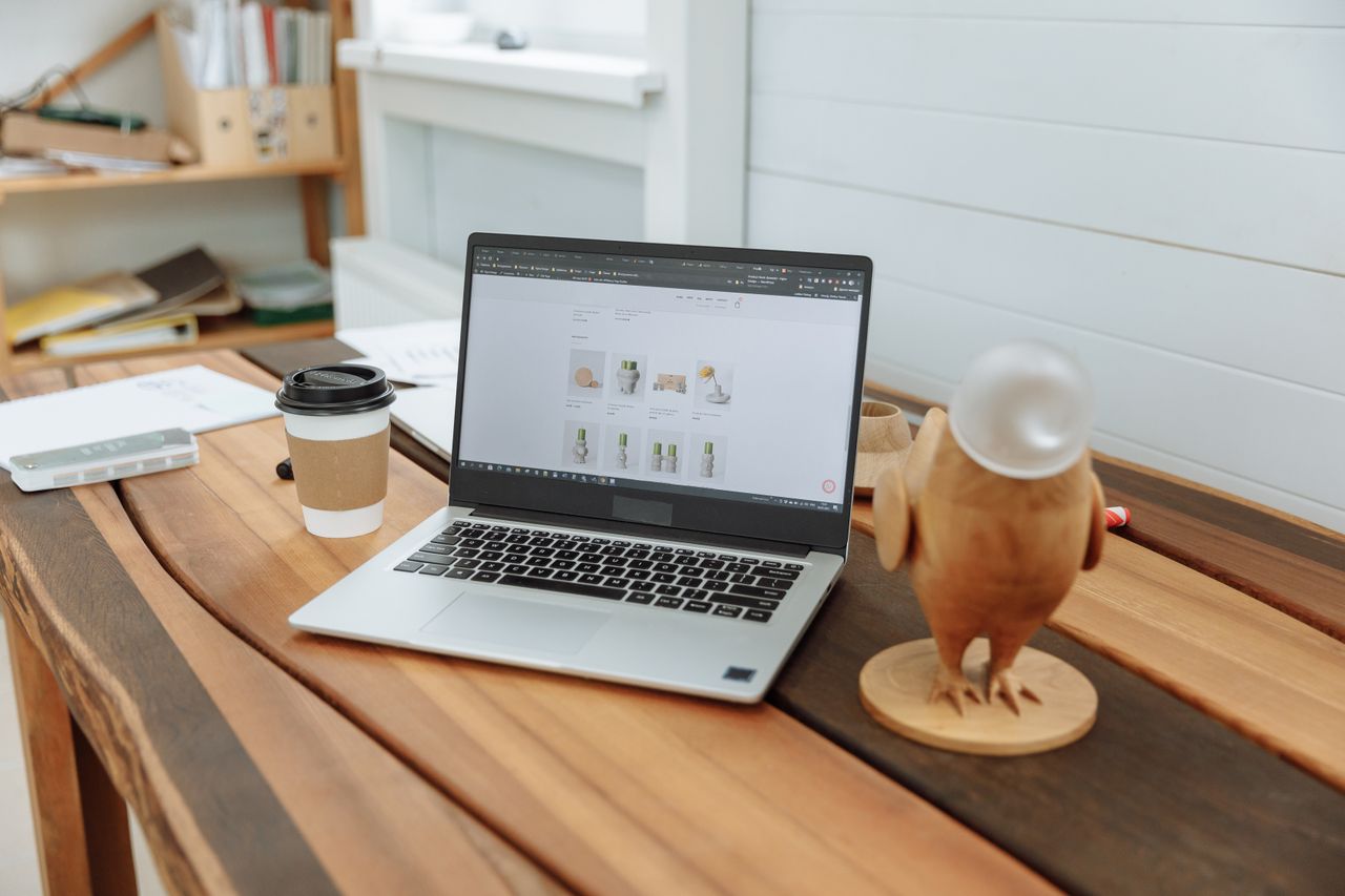 about-04 A contemporary office desk setup featuring a laptop, coffee cup, and wooden figurine on a wooden table.